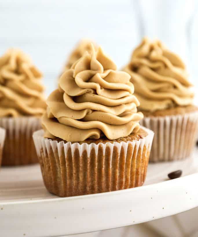 side view of homemade coffee cupcakes, topped with coffee buttercream, served on a white cake stand